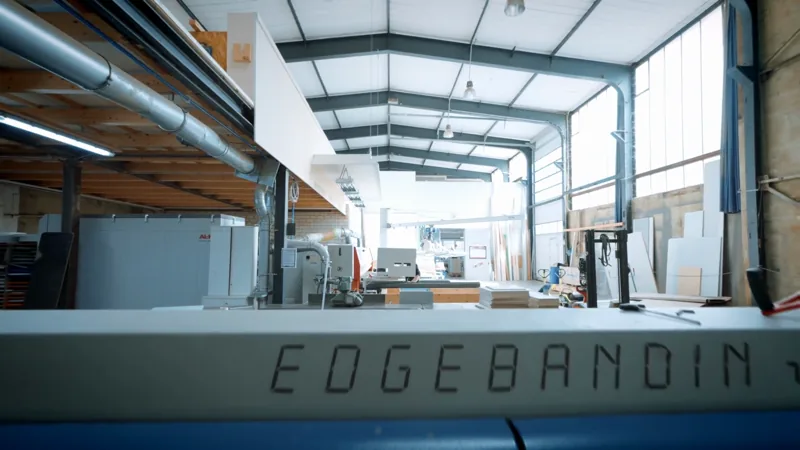 Kantenanleimmaschine im Vordergrund einer hellen Werkhalle